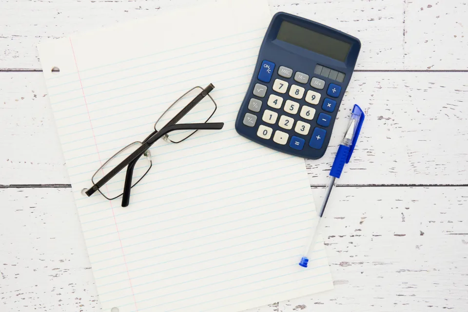 Calculadora, caneta e óculos sobre papel